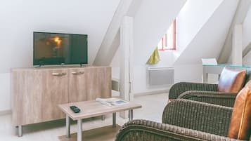Un salon moderne avec un téléviseur posé sur un meuble en bois, une petite table avec une télécommande et un canapé en osier.
