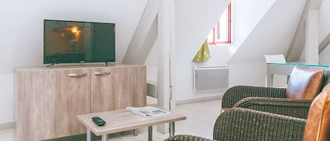 En moderne stue med et fjernsyn på et træskab, et lille bord med en fjernbetjening og en fletsofa.