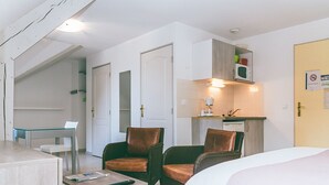 Ein Hotelzimmer mit einem Bett, zwei Sesseln, einem kleinen Tisch mit einer Fernbedienung, einer Küchenzeile mit einer Mikrowelle und einer Badezimmertür.