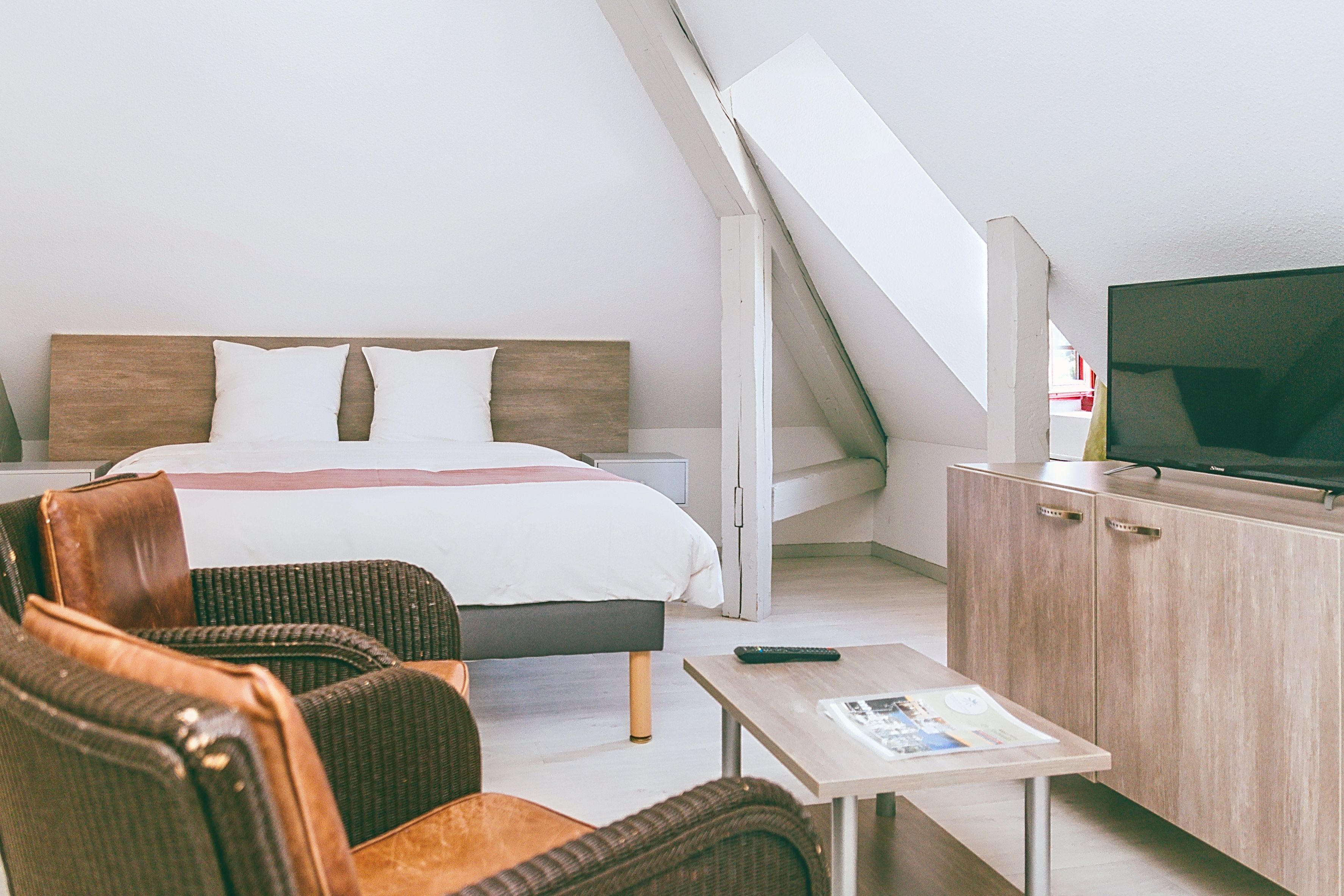 Una habitación de hotel con cama, televisión, una mesita pequeña y una silla de mimbre.