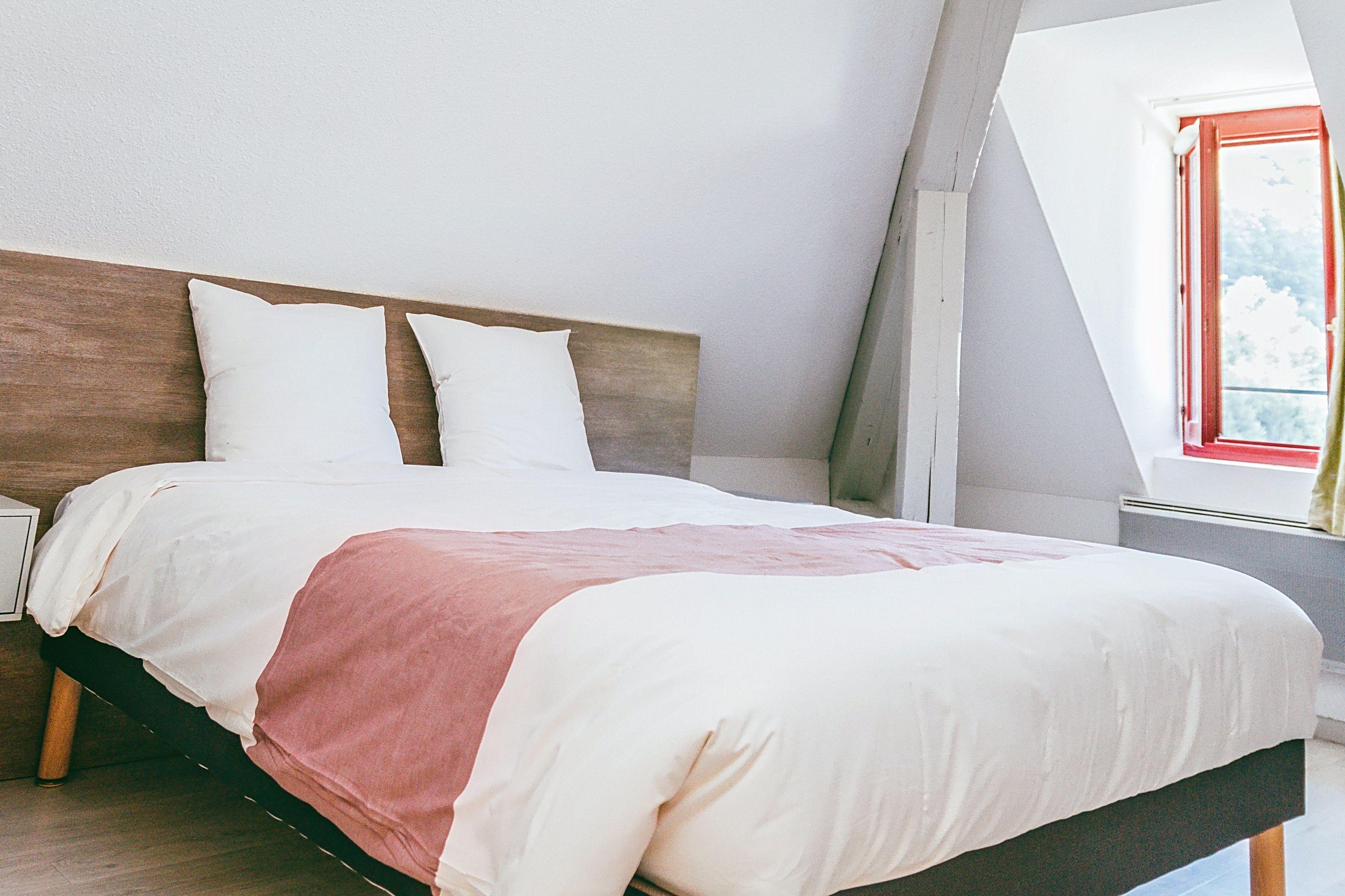 A bed with a wooden headboard, white bedding, and a red accent.