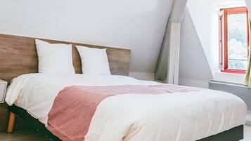 A bed with a wooden headboard, white bedding, and a red accent.