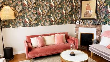 A living room with a patterned wallpaper, a pink sofa, a round coffee table, and a fireplace.