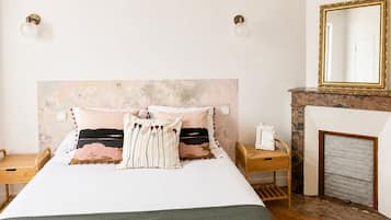 A bedroom with a bed, bedside tables, a mirror, and a fireplace.