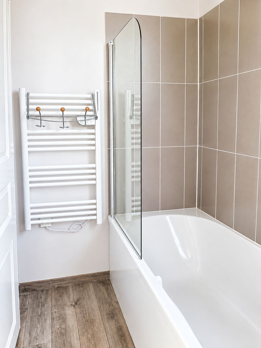 A bathroom with a white bathtub, a glass shower enclosure, and a white towel rack with wooden knobs.