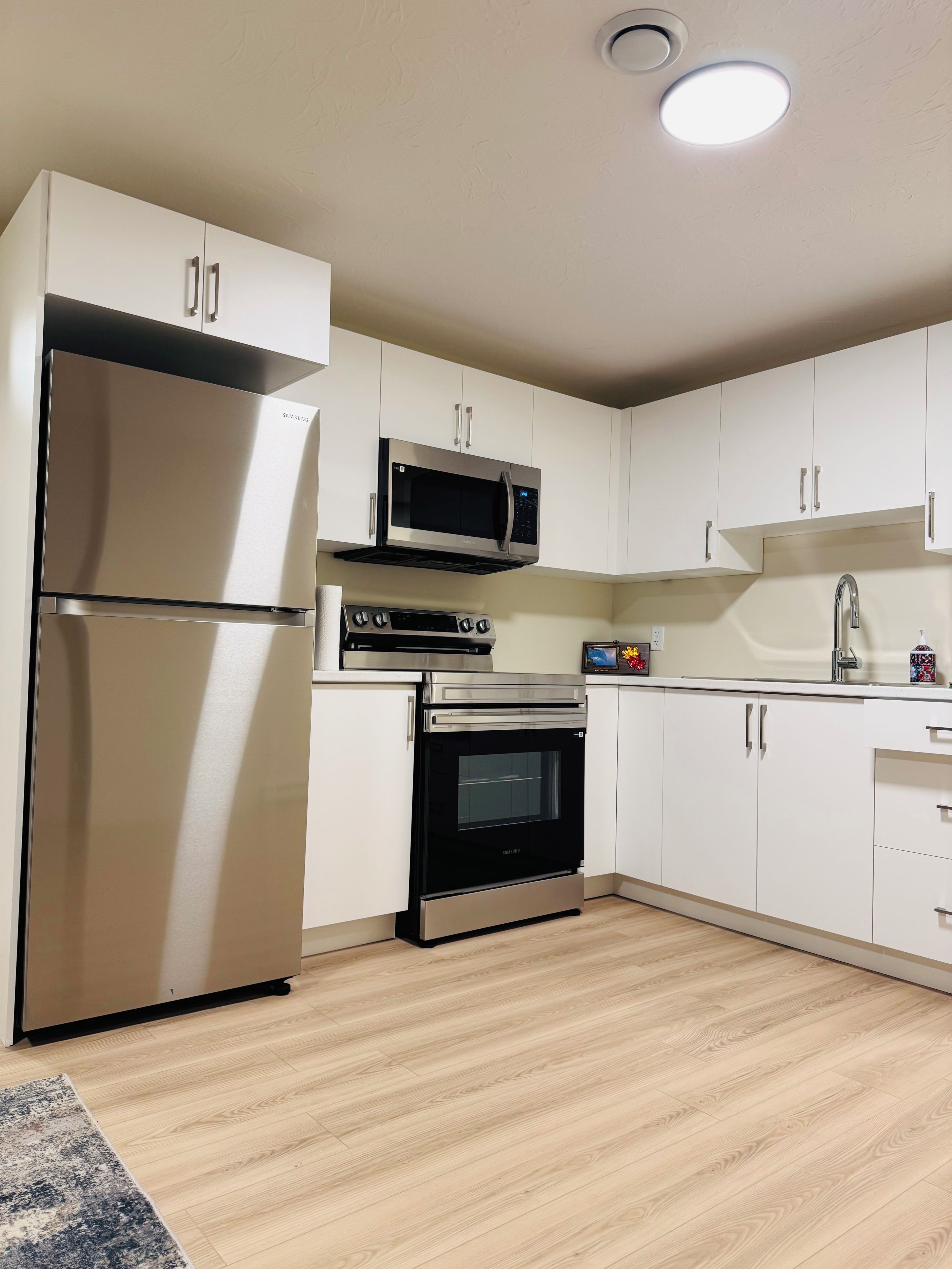A modern kitchen with stainless steel appliances, white cabinetry, and a wooden floor.
