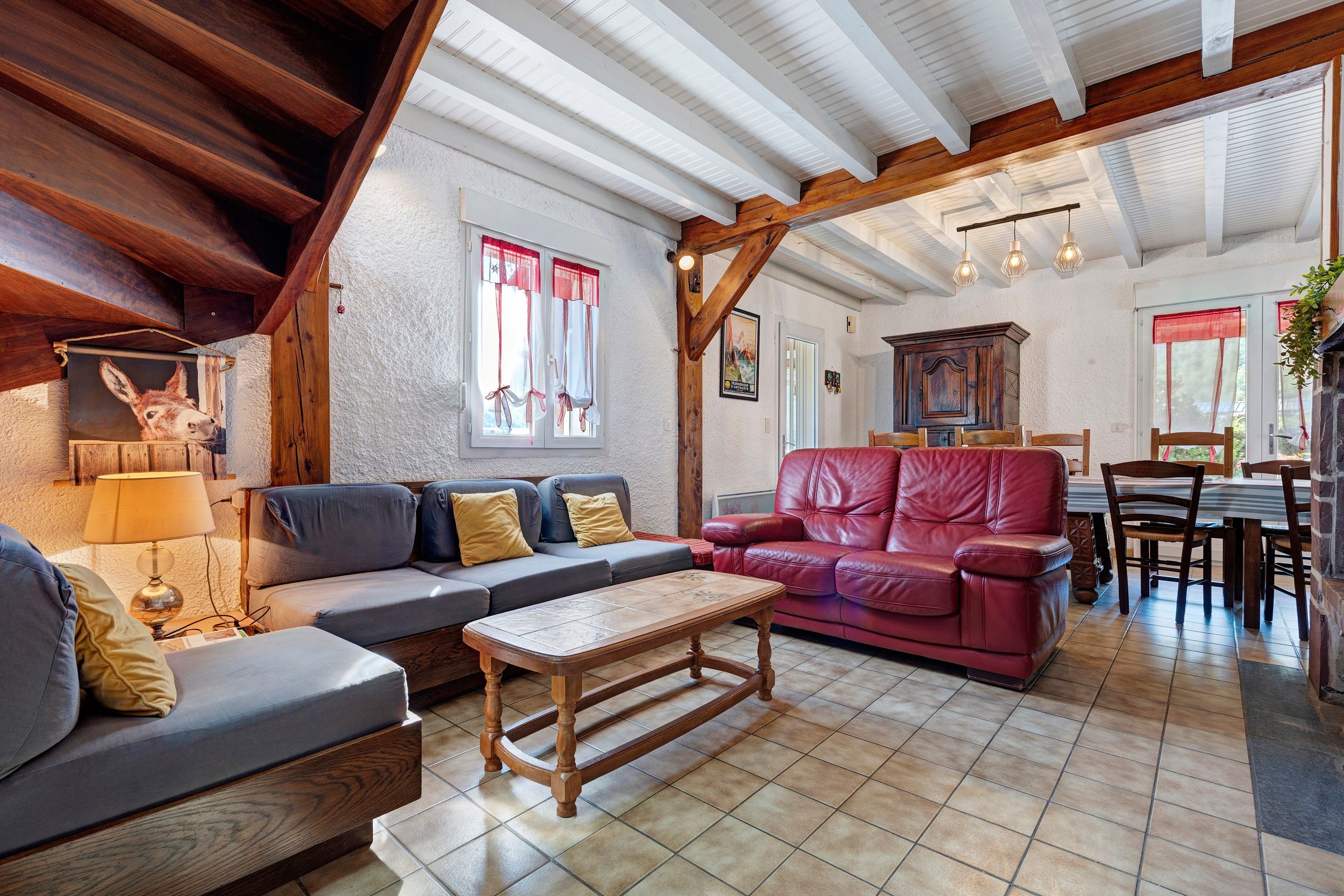 A cozy living room with a wooden ceiling, a grey sofa, a red leather couch, and a wooden coffee table.