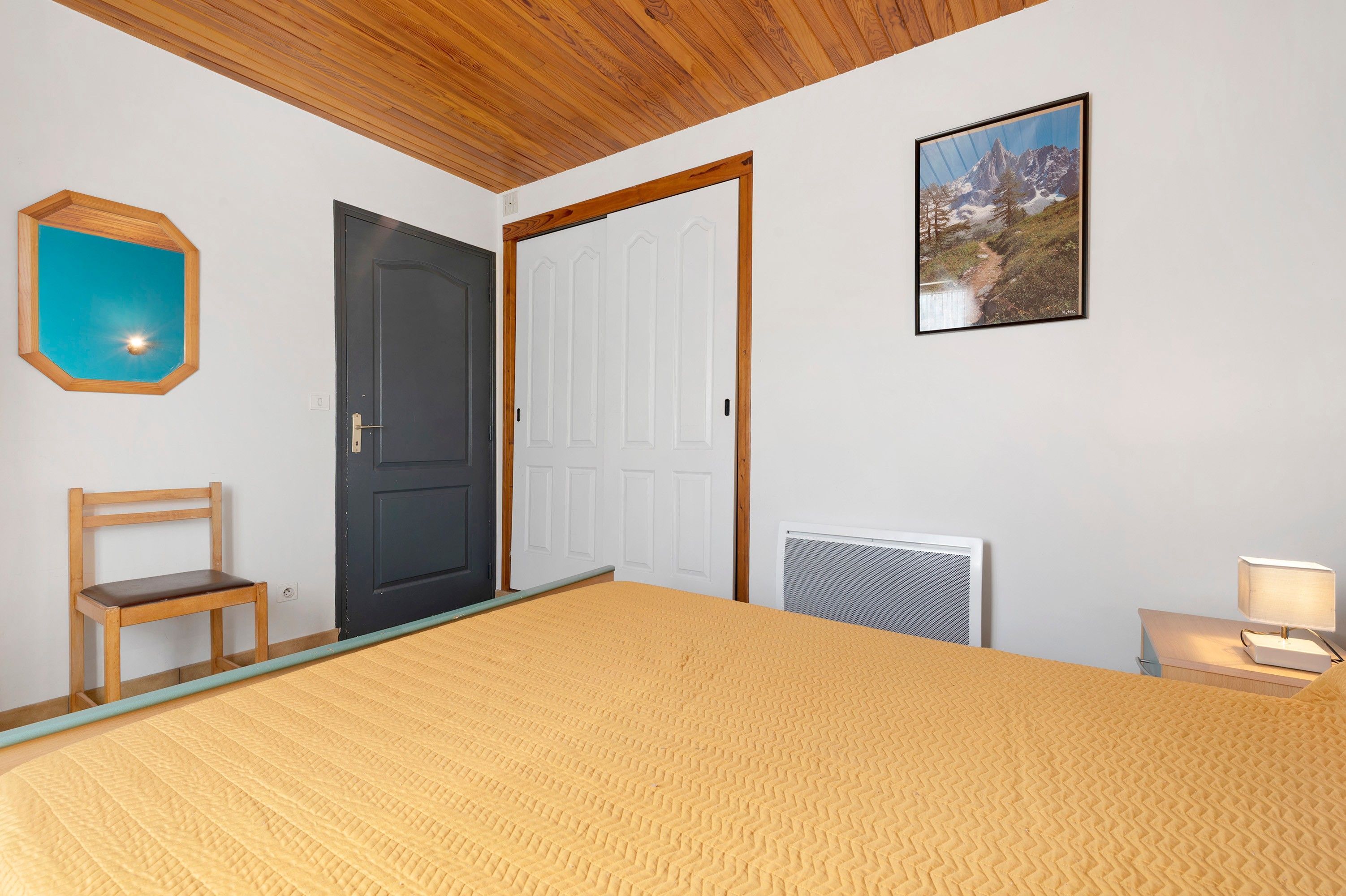 A bedroom with a bed, a chair, a door, a radiator, and a framed picture on the wall.