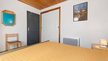 A bedroom with a bed, a chair, a door, a radiator, and a framed picture on the wall.