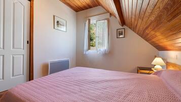 Una camera da letto con soffitto spiovente, un letto con copripiumino rosa, una finestra con vista e una lampada da comodino.