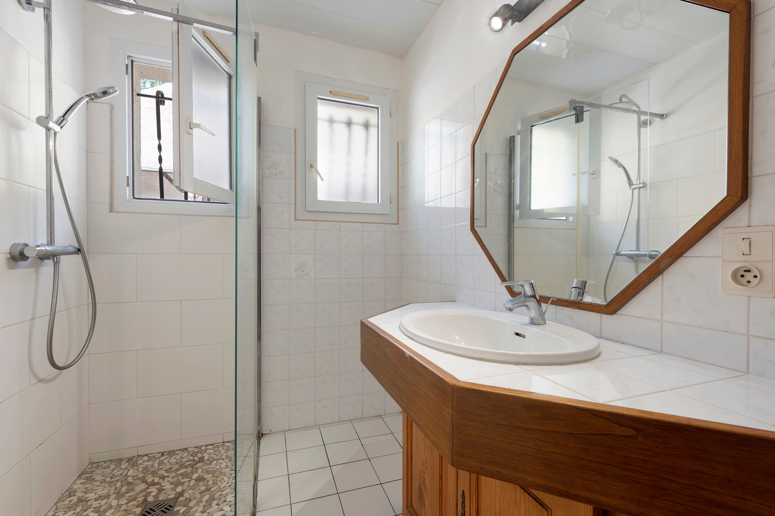 Een badkamer met een douche, wastafel en spiegel.