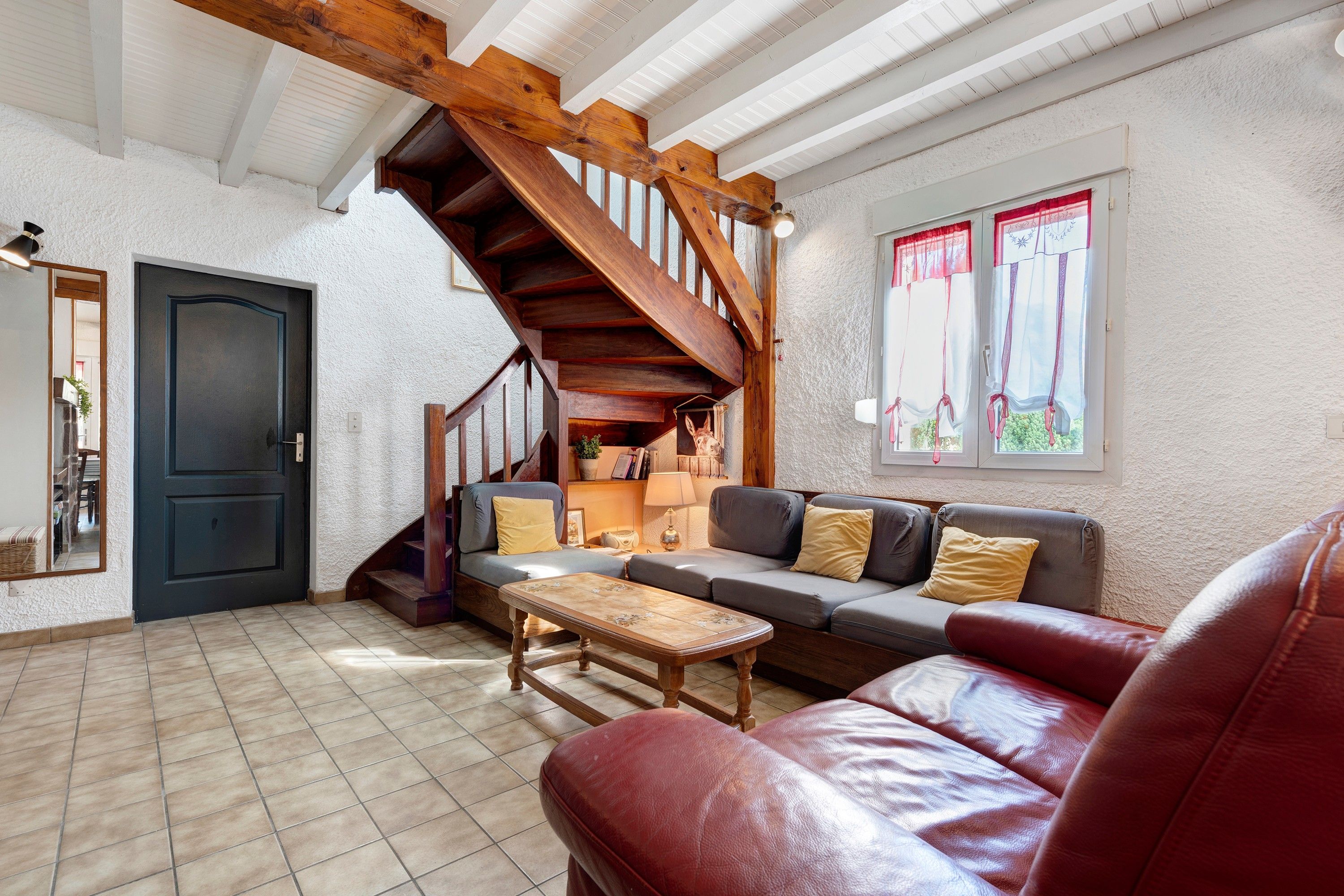A cozy living room with a wooden staircase, a sofa set, a coffee table, and a red leather couch.