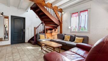 A cozy living room with a wooden staircase, a sofa set, a coffee table, and a red leather couch.