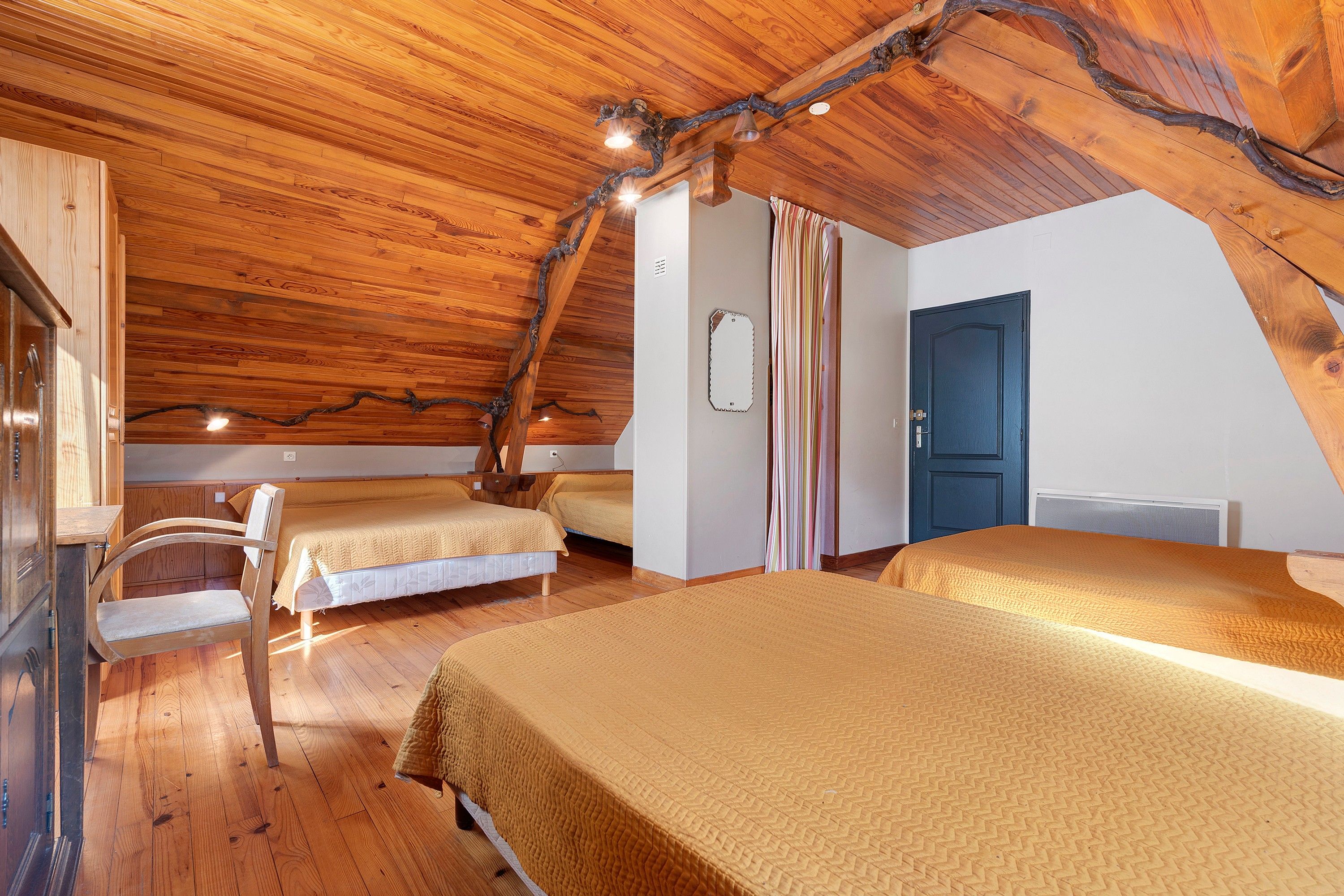 A cozy attic bedroom with wooden beams, two beds, a chair, and a door.