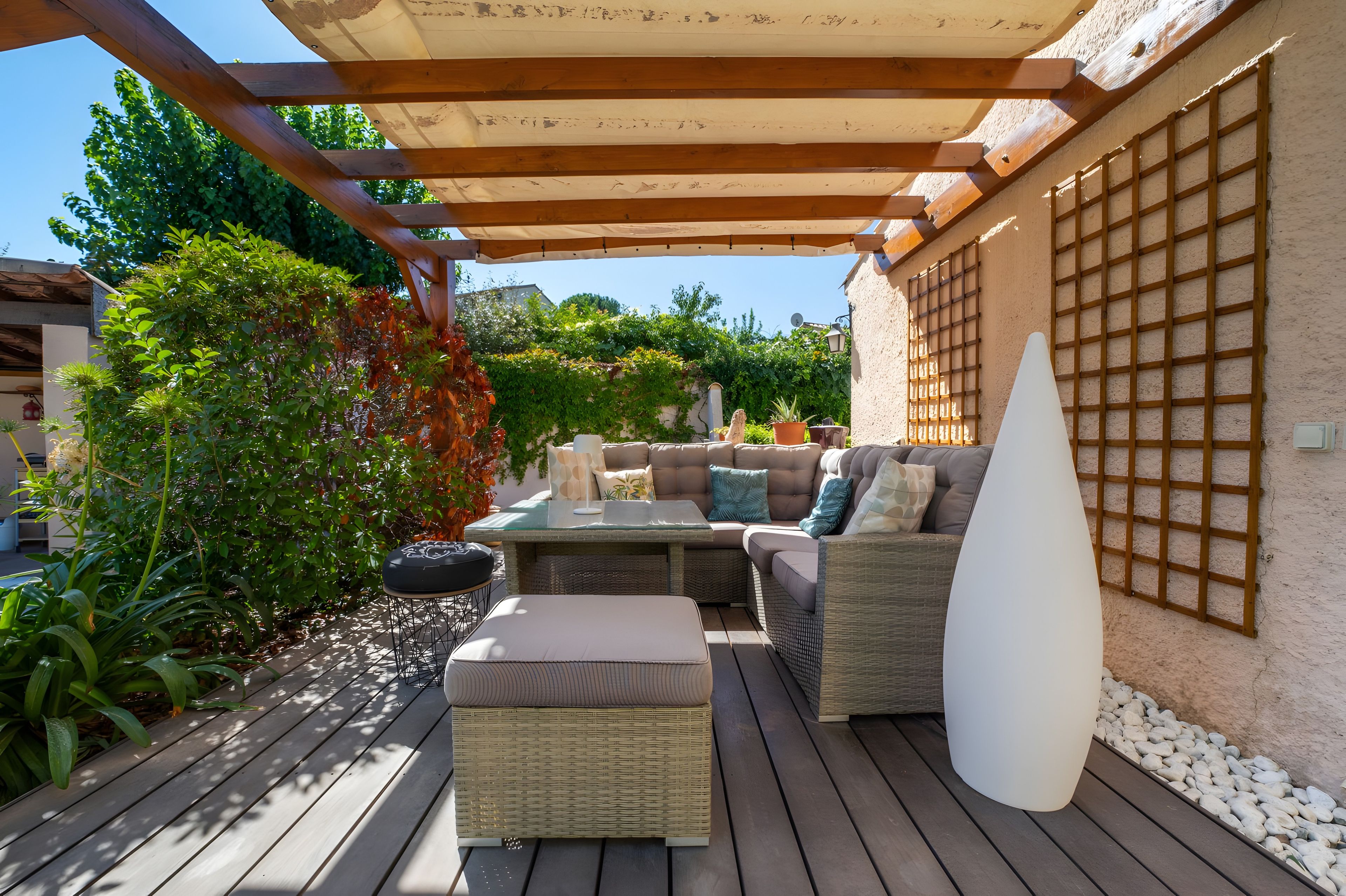 An outdoor patio with a wooden pergola, wicker furniture, and a white conical light fixture.