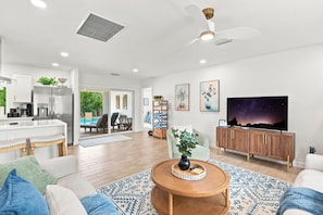 Un salon moderne doté d’un téléviseur à écran plat, d’un ventilateur de plafond et d’un coin repas avec vue sur la piscine.