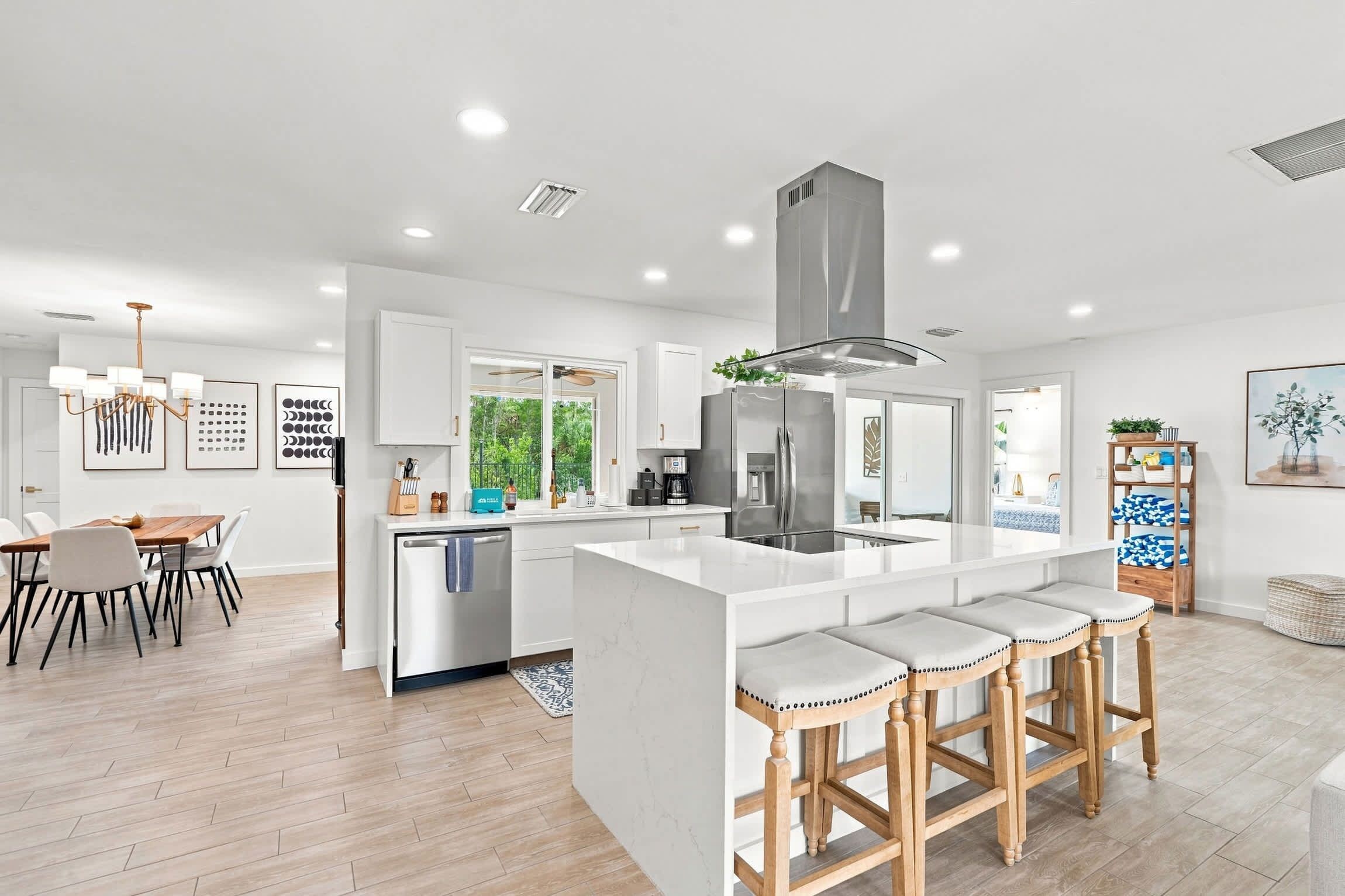 A modern kitchen with a central island, bar stools, and a dining area with a table and chairs.