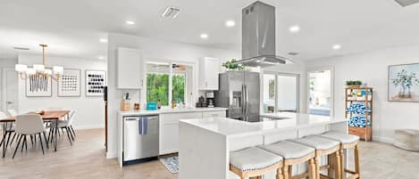 A modern kitchen with a central island, bar stools, and a dining area with a table and chairs.