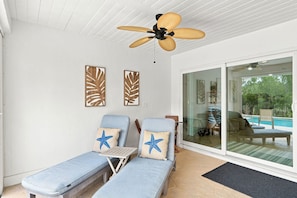 A sunlit room with a ceiling fan, two lounge chairs with starfish pillows, and a glass door leading to a pool area. - Upscale Bonita Springs  Pool, Spa & Privacy (Bonita Springs)