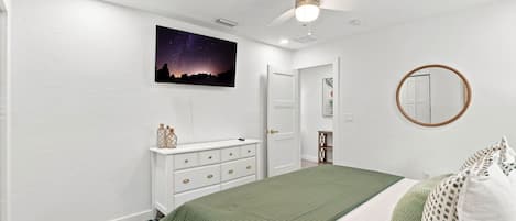 Une chambre à coucher comprenant un lit, une commode, un ventilateur de plafond, une décoration murale représentant un ciel étoilé et un miroir rond.
