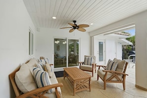 Une terrasse ensoleillée avec un ventilateur de plafond, une table en bois et des chaises rembourrées.