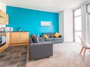 Ein modernes Wohnzimmer mit Küche, grauem Sofa und Essbereich.
