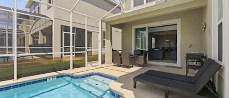 A residential pool area with a hot tub, lounge chairs, and a covered patio.