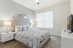 A bedroom with a bed, two bedside tables with lamps, a large window with blinds, and a TV on a stand. - 5-bedroom Family House With Pool and Themed Rooms (Kissimmee)