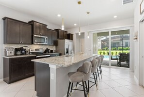 A modern kitchen with dark cabinetry, stainless appliances, and a large island with bar stools. - Chic Retreat in Orlando With Pool and Game Room (Clermont)