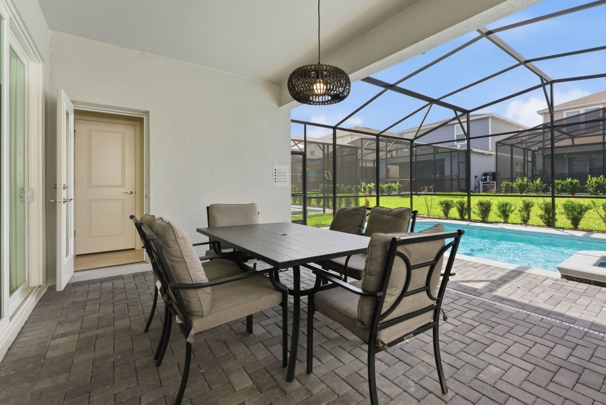 A patio with a table and chairs, a pool, and a covered area with a view of the neighborhood.