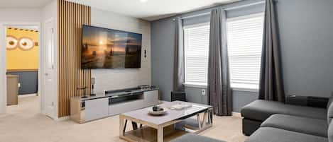 Una sala moderna con televisor de pantalla plana, una zona de comedor con mesa y sillas, y una cocina con horno empotrado.