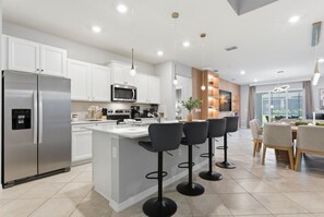 A modern kitchen with stainless steel appliances, a central island with bar stools, and a dining area with a view. - Luxury Themed Villa With Pool and Cinema (Clermont)