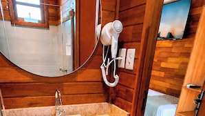 A bathroom with a wooden interior, a sink, a mirror, a hairdryer, and a television. - Chalés Eco Thermas (Tupã)