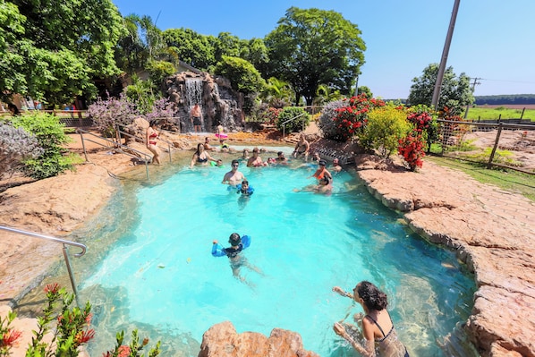 A swimming pool with clear water, surrounded by rocks and greenery.
