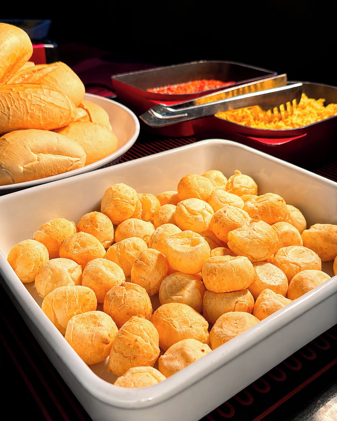 A buffet table with a variety of food items including bread rolls, cheese, and a dish that appears to be a casserole.