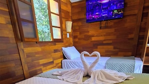 A hotel room with a wooden interior, a bed with white bedding, a heart-shaped towel arrangement, and a TV mounted on the wall. - Chalés Eco Thermas (Tupã)