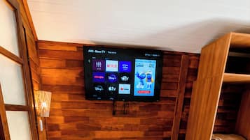 A hotel room with a bed, a television mounted on the wall, a wooden wardrobe, and a small table.