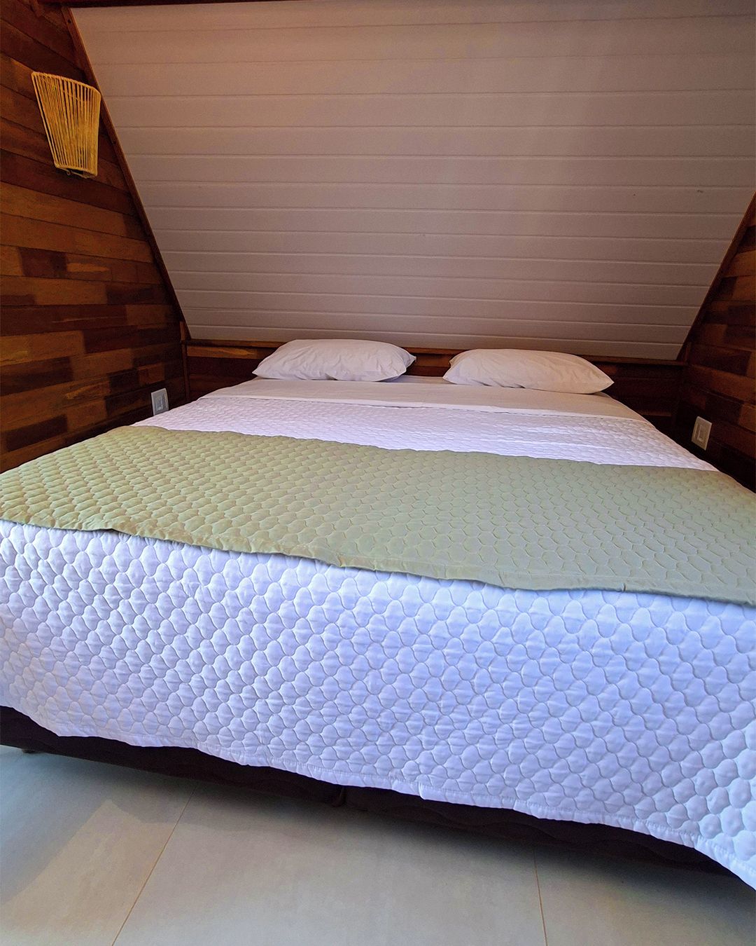 A single bed in a room with wooden walls and a sloped ceiling.