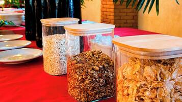 A table with three glass containers of different food items, a black coffee pot, and a red tablecloth.
