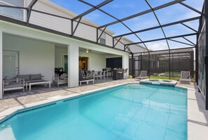 Una piscina con un patio cubierto, mobiliario exterior y una parrilla.