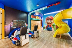 A room with a gaming setup including a racing game on a TV, a Mario-themed play area, and a yellow slide. - Luxury Villa With 10 Bedrooms - Pool, Themed Rooms (Clermont)