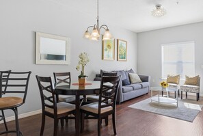 A dining area with a round table and chairs, a sofa, and a coffee table with a vase of flowers. - Disney Area 3BR Townhome + Resort Amenities (Kissimmee)
