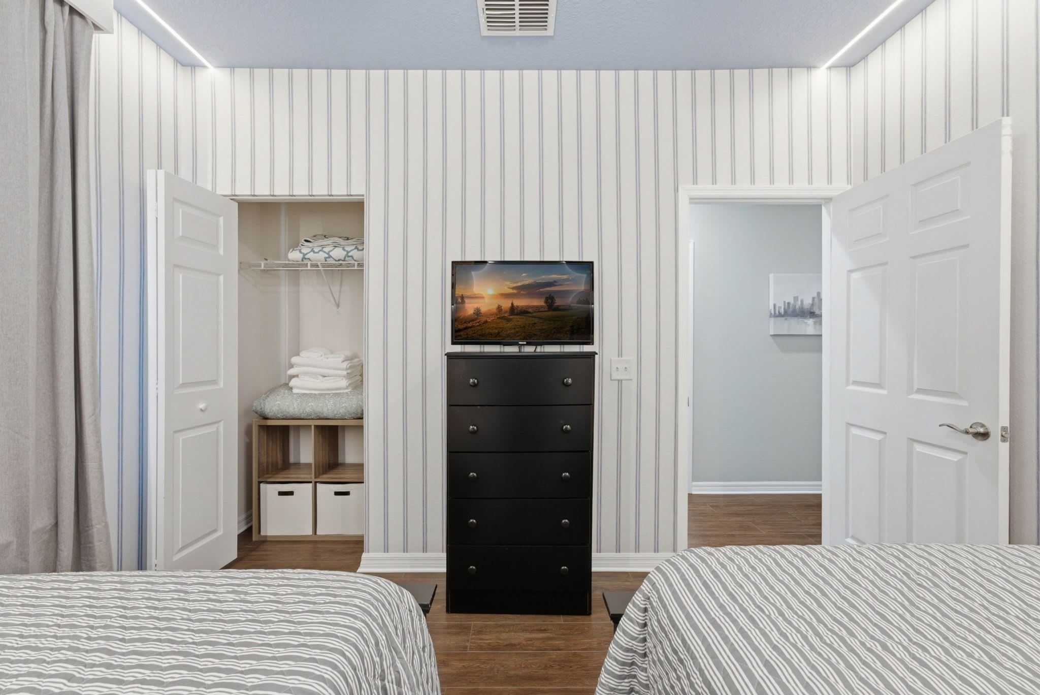 A bedroom with two beds, a dresser, a television, and a closet with folded clothes.
