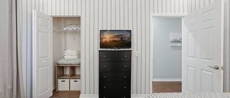 Une chambre avec deux lits, une commode, un téléviseur et un placard contenant des vêtements pliés.