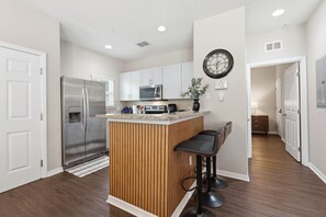 A modern kitchen with a central island, stainless steel appliances, and a clock on the wall. - West Lucaya 4BR Home Near Disney & Parks (Kissimmee)