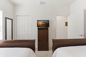 A bedroom with two beds, a TV on a wooden stand, and white doors. - West Lucaya 4BR Townhome Near Disney (Kissimmee)