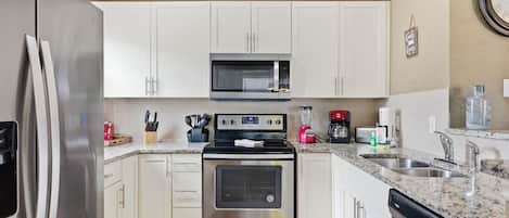 Una cocina moderna con electrodomésticos de acero inoxidable, armarios blancos, encimera de granito y lavavajillas integrado.