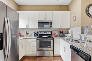 A modern kitchen with stainless steel appliances, white cabinetry, a granite countertop, and a built-in dishwasher. - West Lucaya 4BR Townhome Near Disney (Kissimmee)
