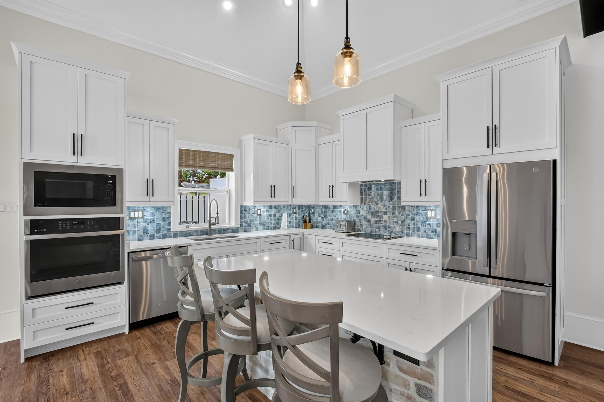A modern kitchen with white cabinetry, stainless steel appliances, a central island with bar stools, and a blue-tiled backsplash.