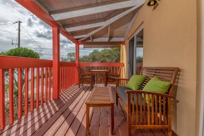 Una terrassa de fusta amb barana vermella, una taula i dues cadires de fusta amb coixins.